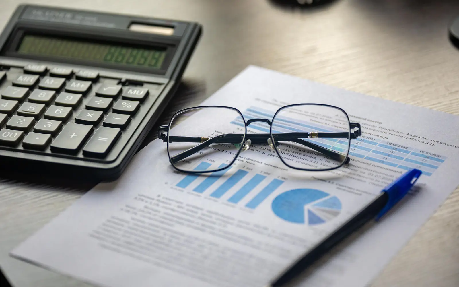 A calculator, spectacles and a printed cost report on a desk