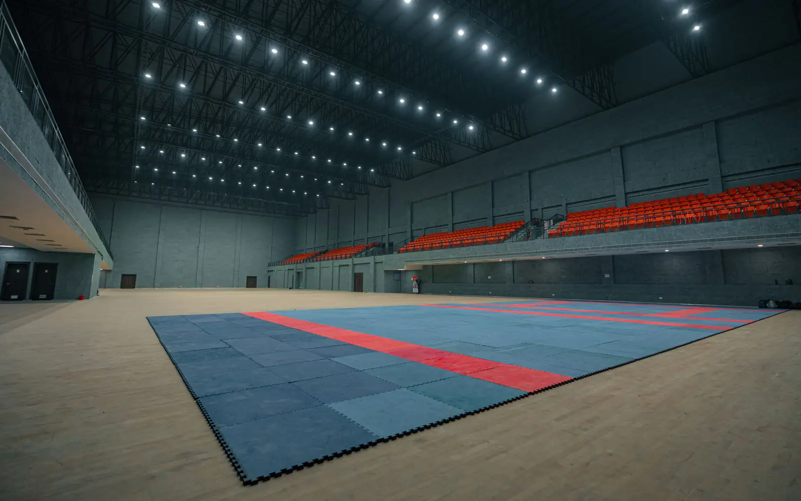 An empty indoor sports hall with tiered seating and matted flooring