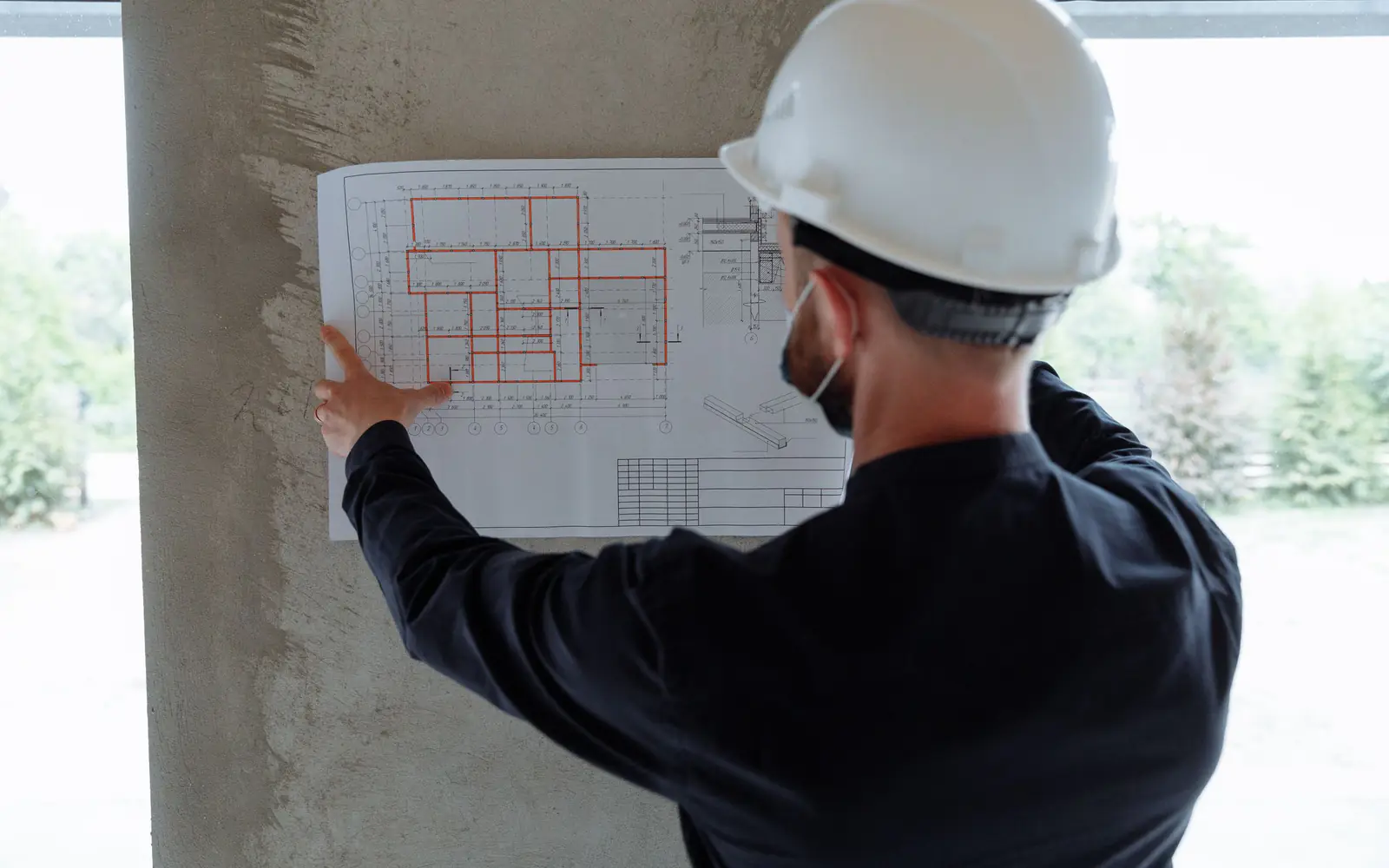 An engineer in a hard hat holding a construction drawing up against a column